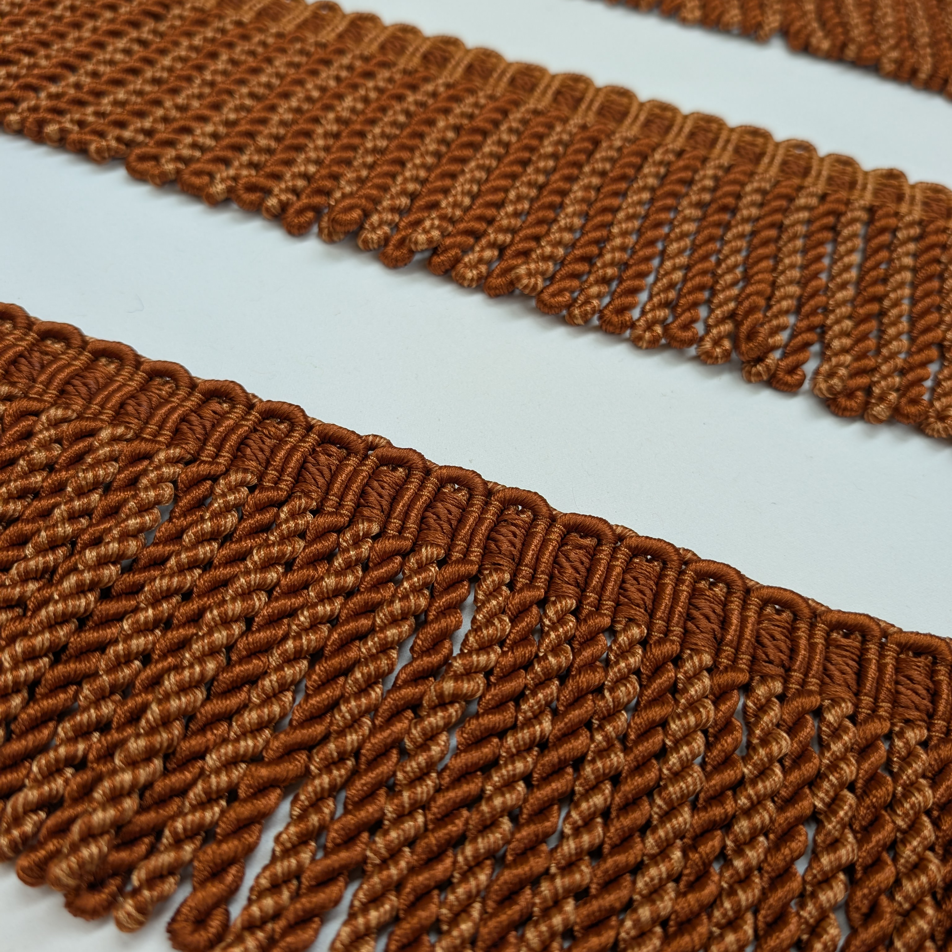 Close-up of brown woven fringes on a light gray background