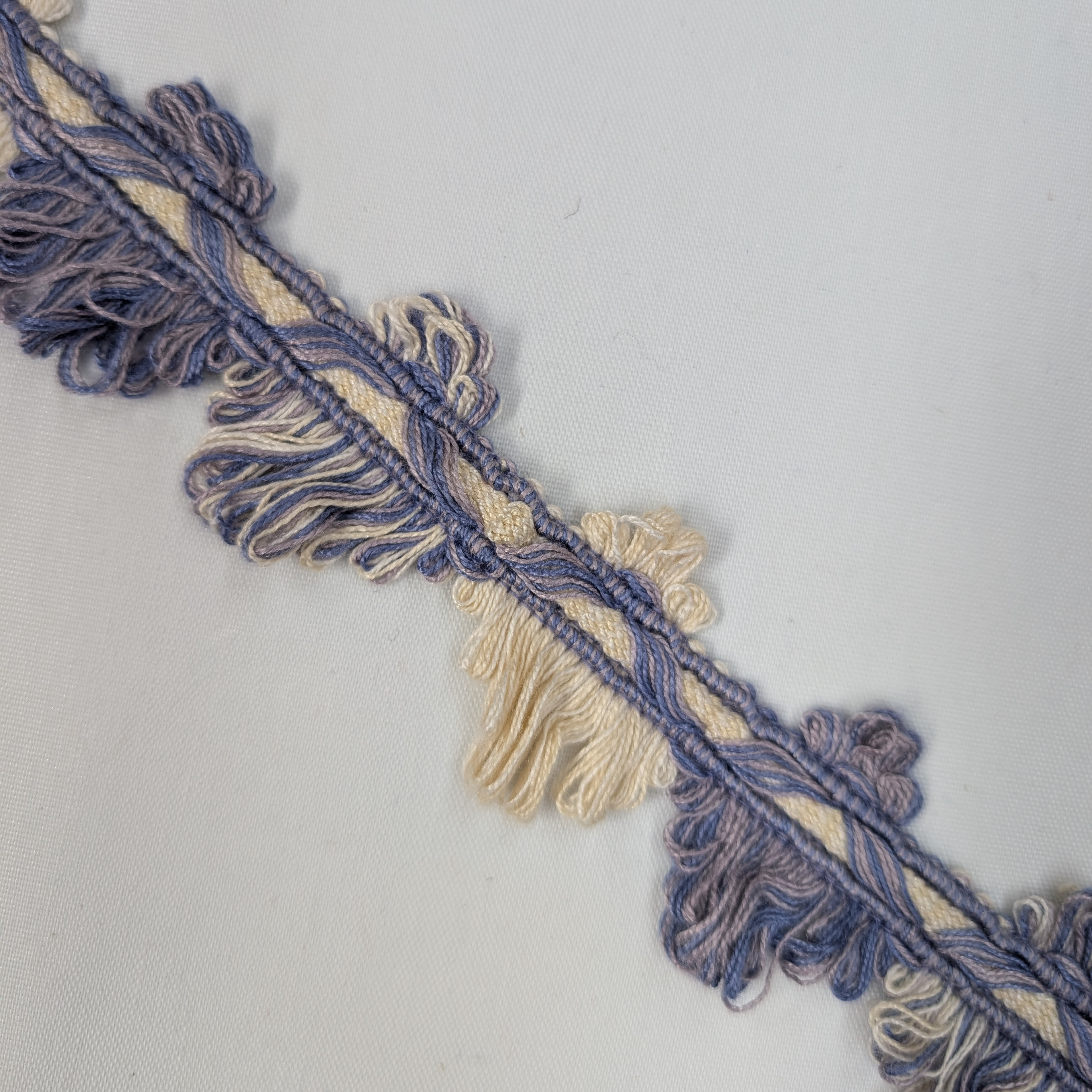 Decorative trim with blue and beige fringes on a light gray background