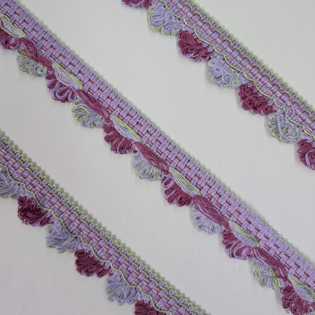 Decorative border trim with purple and pink tassels on a white background