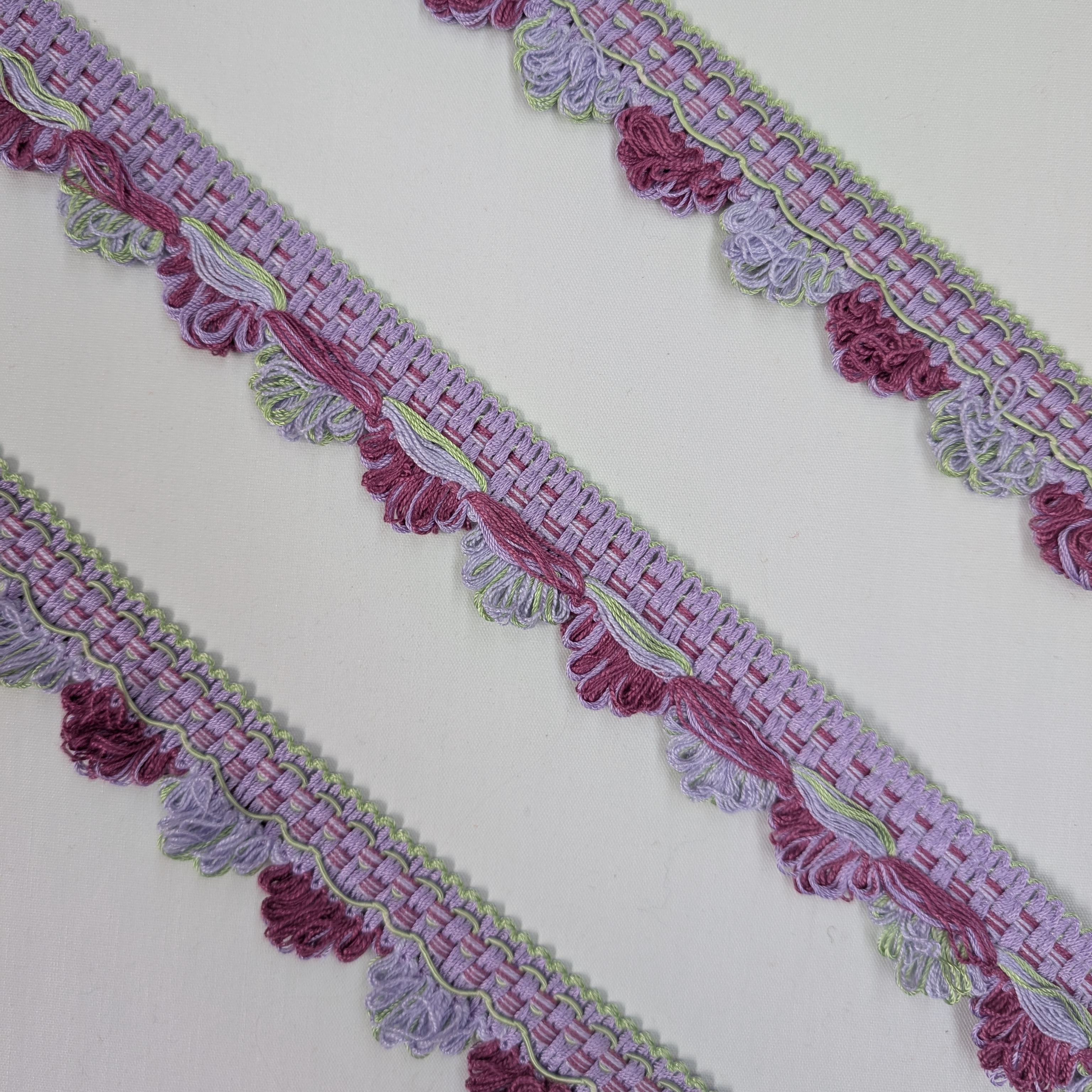 Decorative border trim with purple and pink tassels on a white background