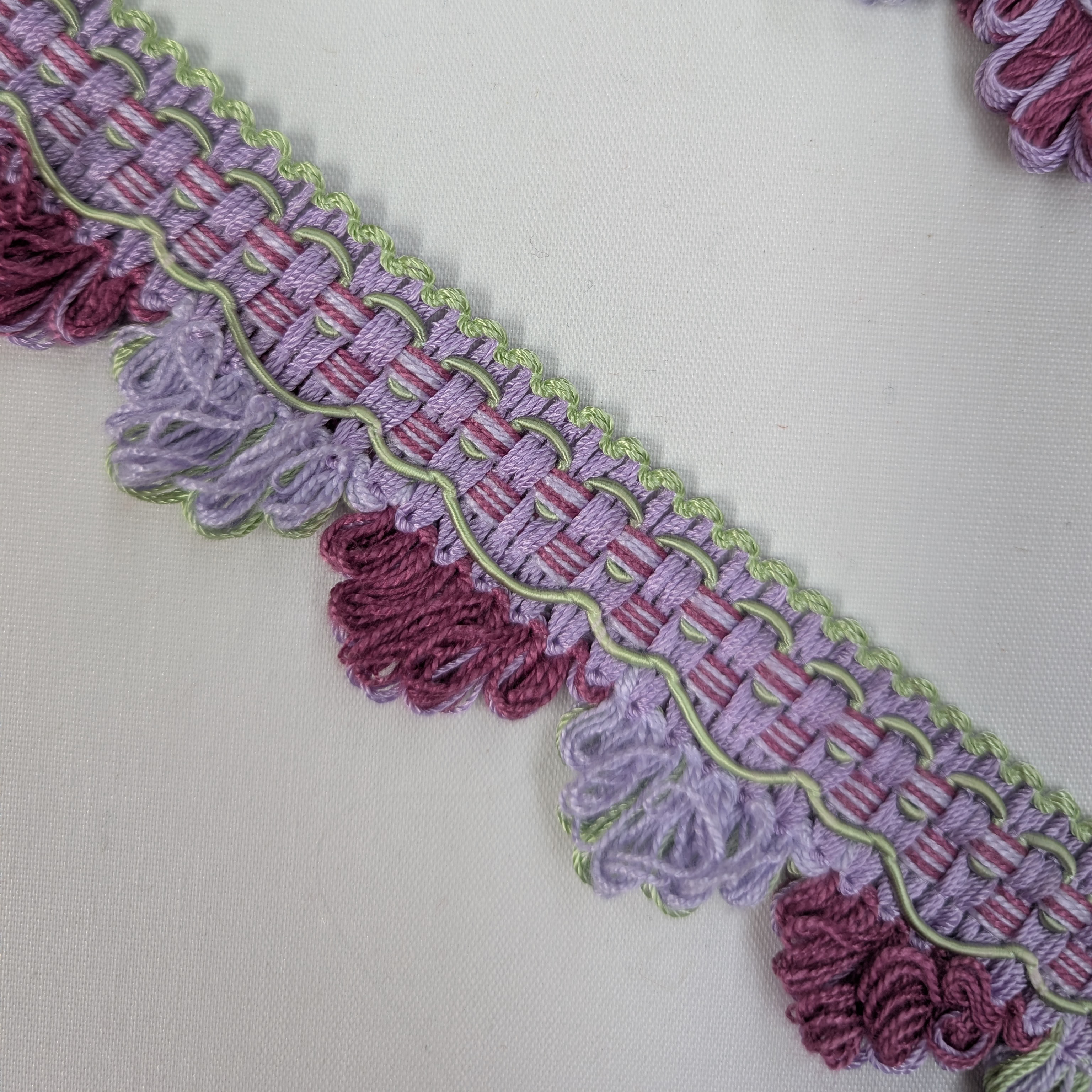 Close-up of a decorative trim with purple and pink fringes on a white background