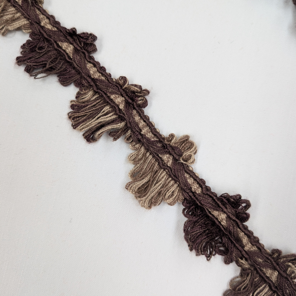 Close-up of brown and beige fringed fabric trim on a white background