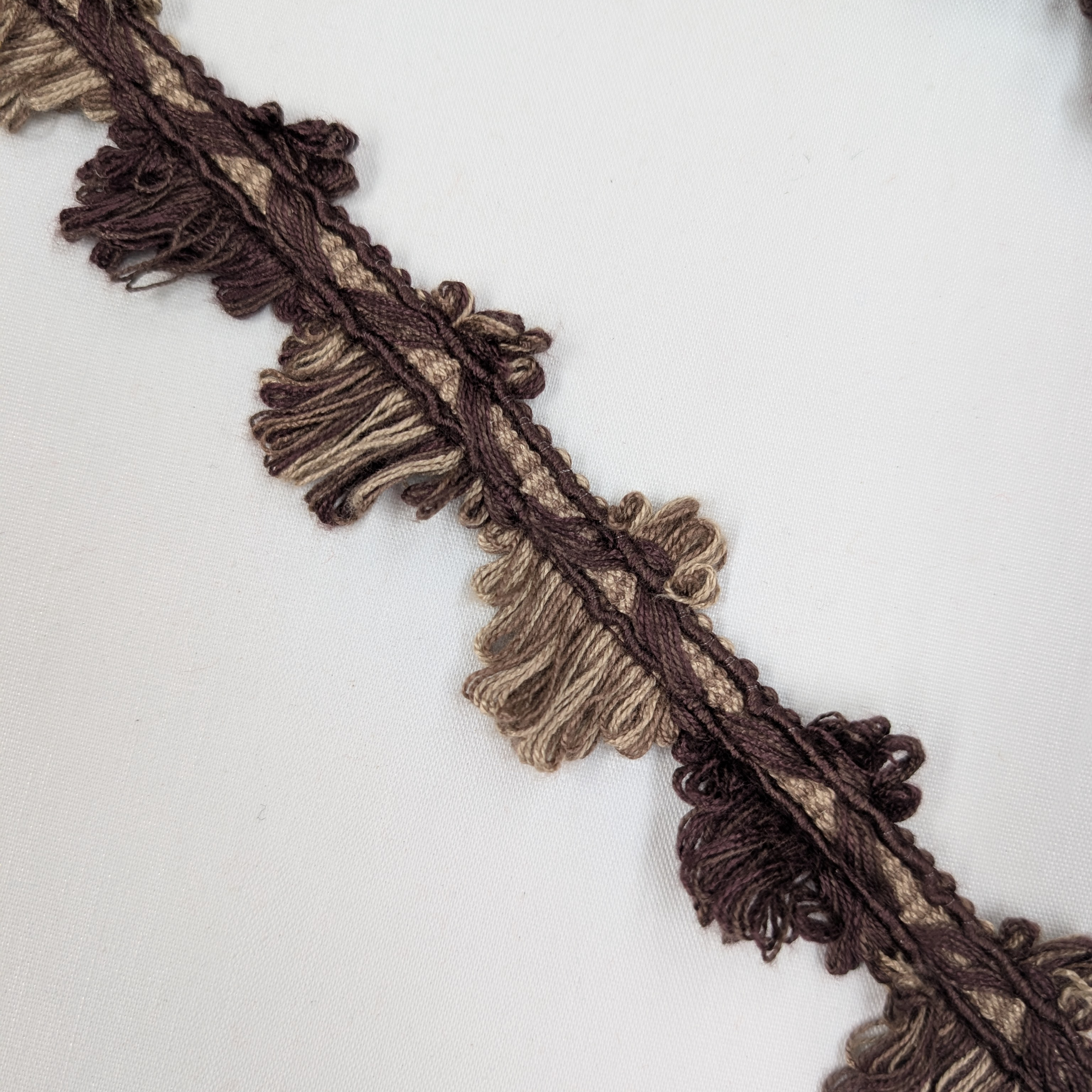 Close-up of brown and beige fringed fabric trim on a white background