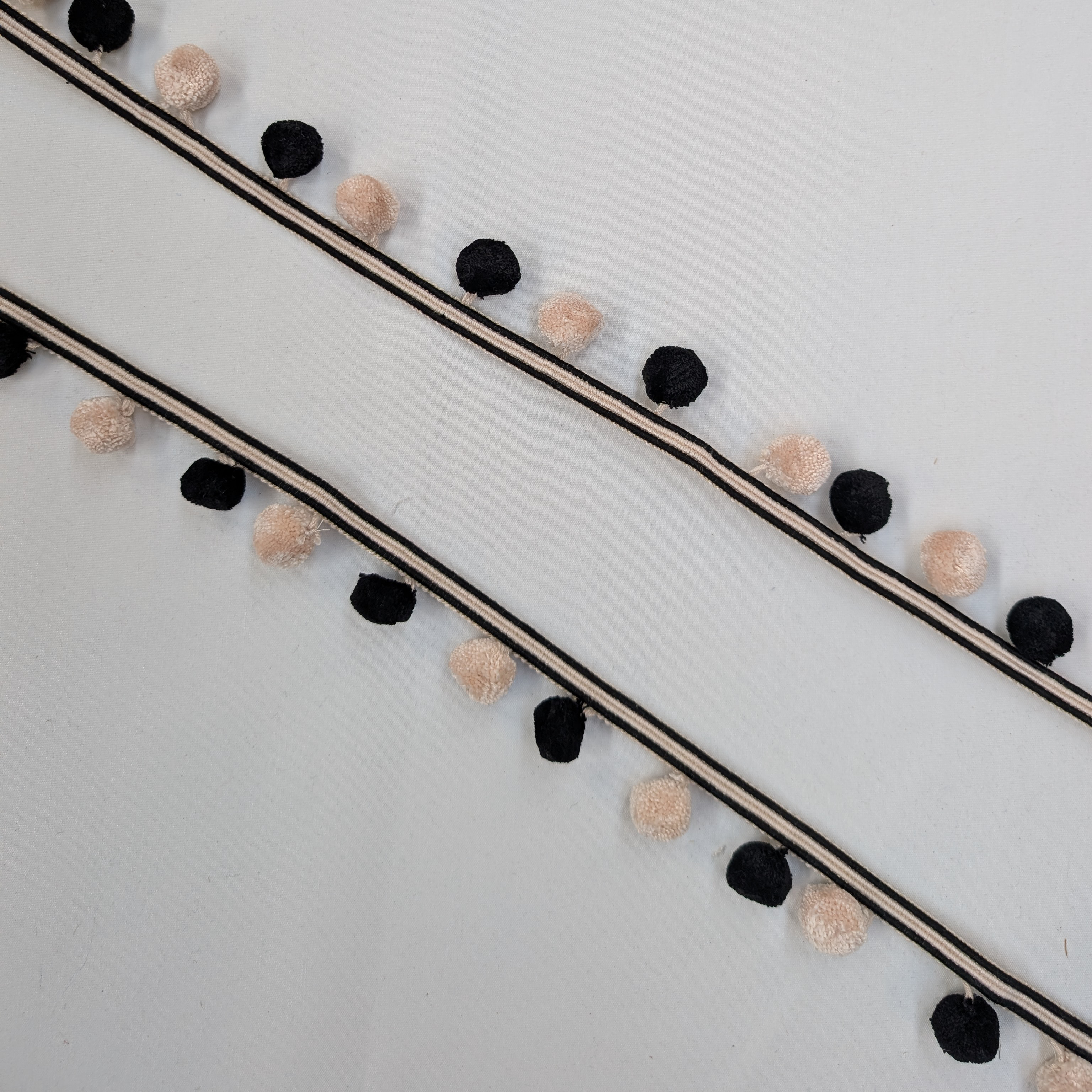 Decorative string with black and beige pom-poms on a light gray background