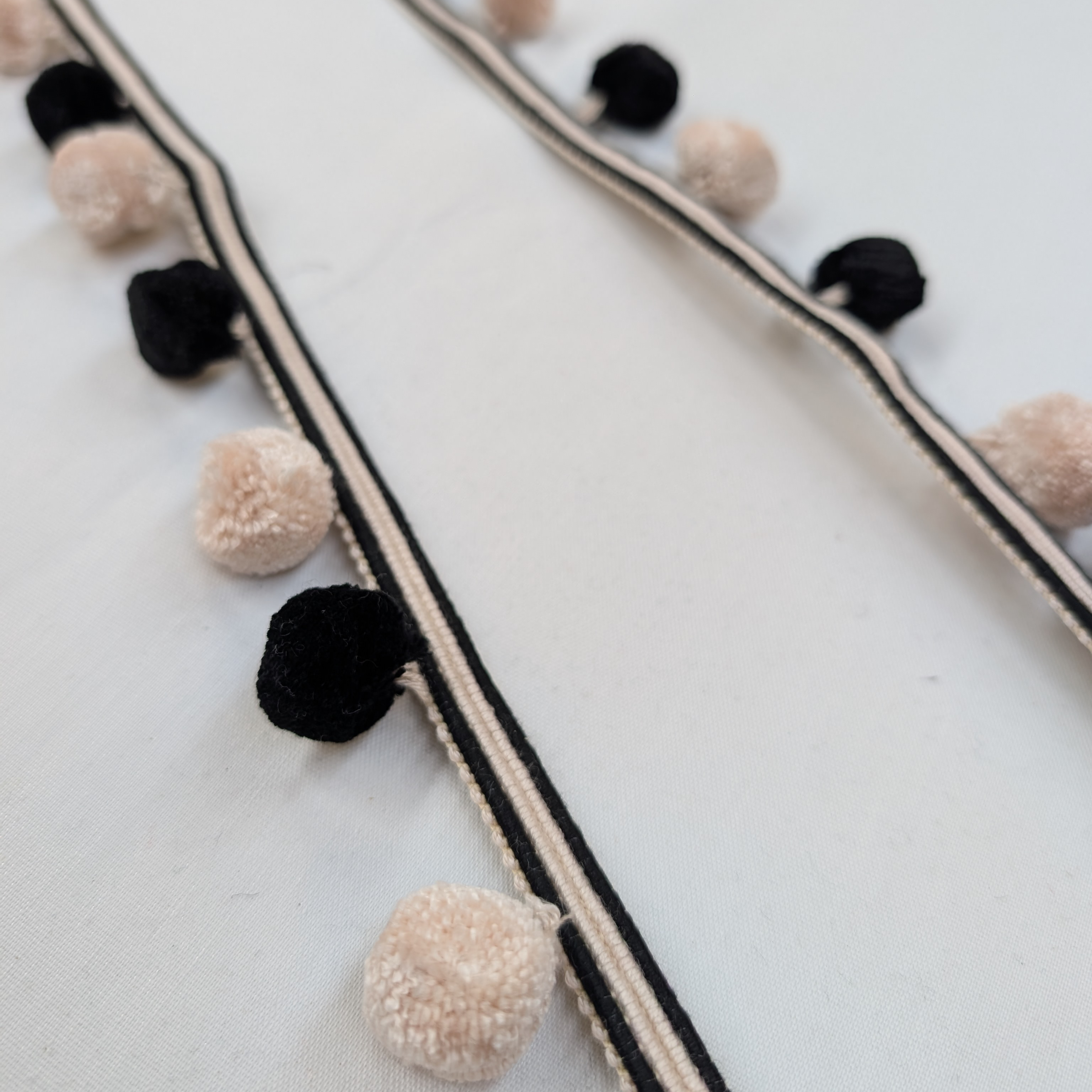 Pom-pom garland with black and beige pom-poms on a white background
