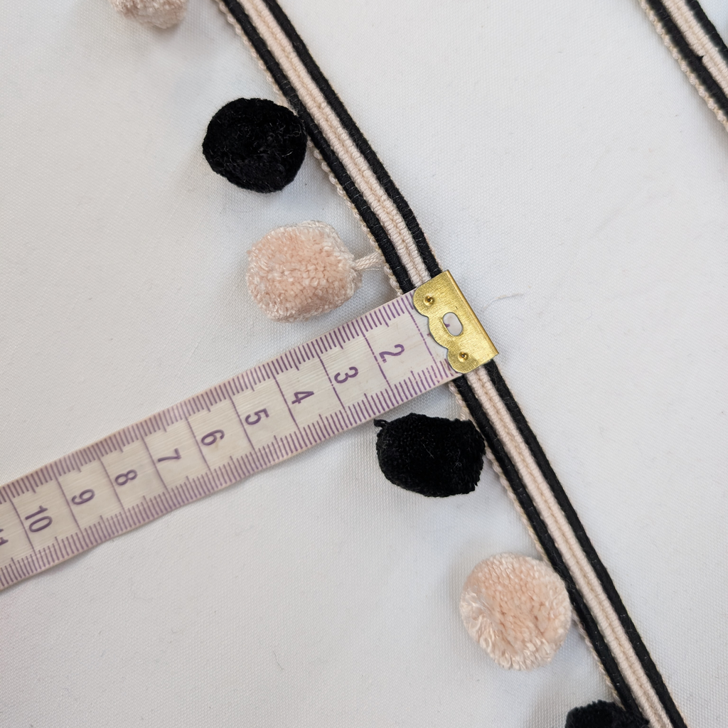 Decorative trim with pom-poms and a measuring tape on a light background