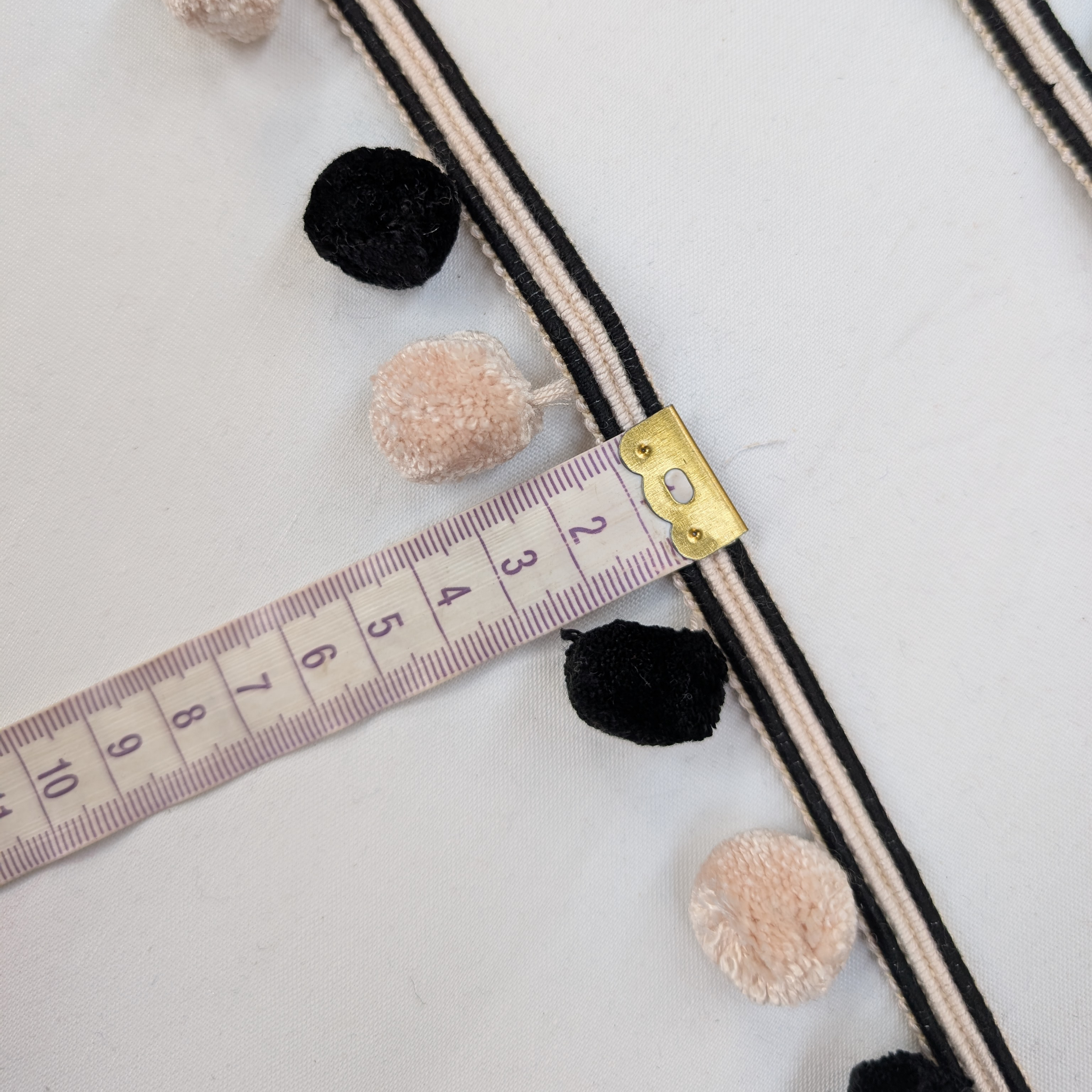 Decorative trim with pom-poms and a measuring tape on a light background