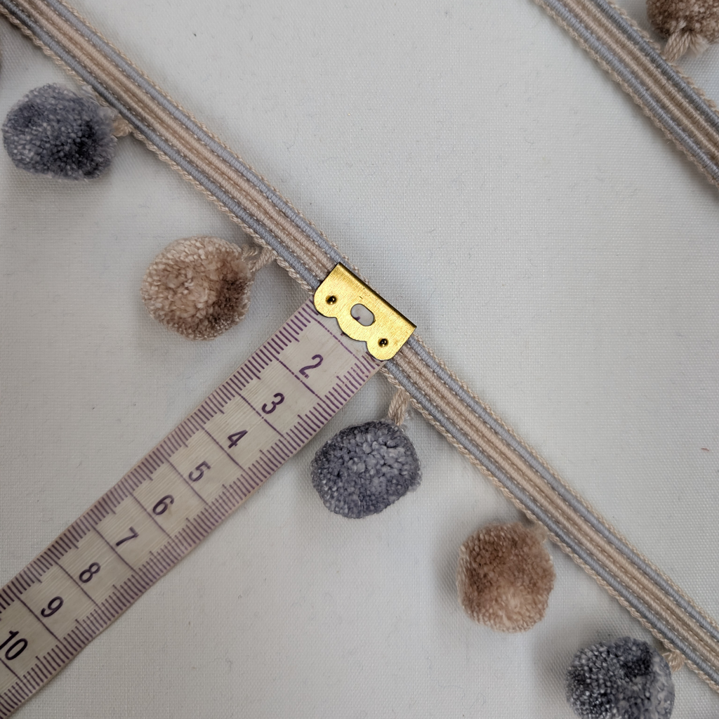 Decorative ribbon with pom-poms and a gold clasp on a white background