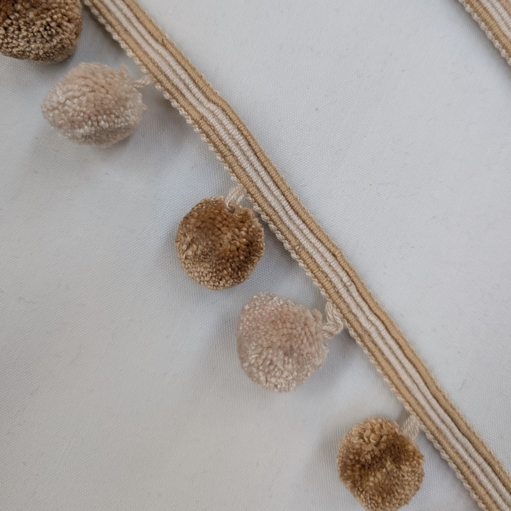 Close-up of decorative trim with brown pom-poms on a white background