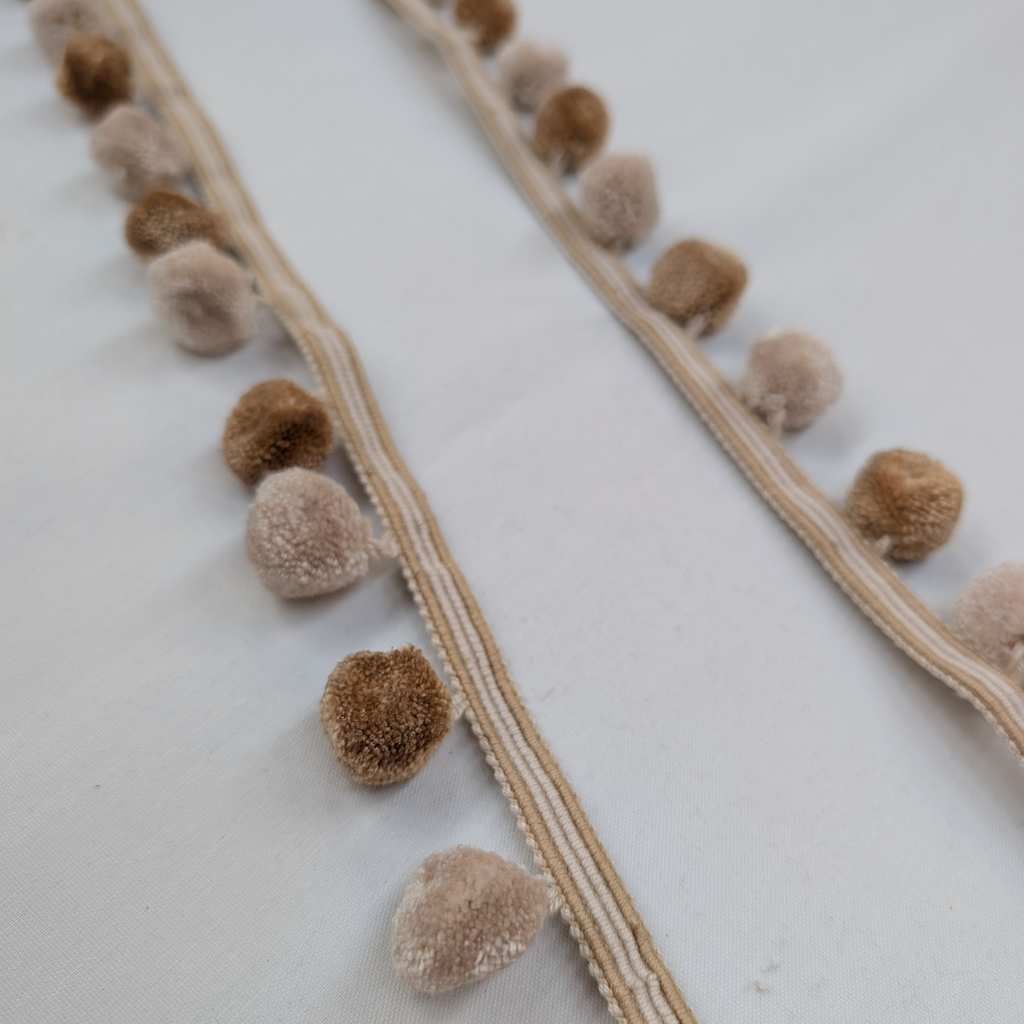 Close-up of a decorative trim with brown pom-poms on a white background