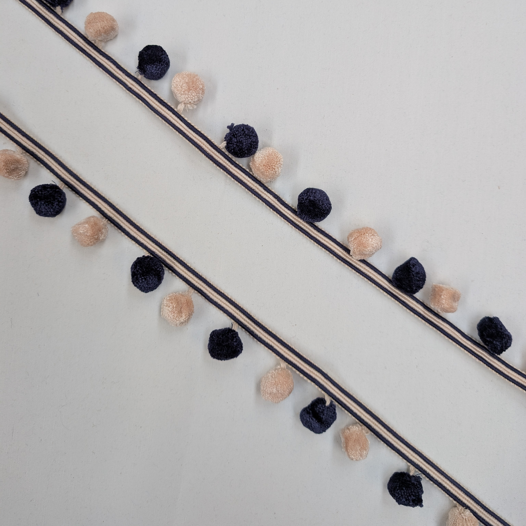Decorative ribbon with navy and beige pom-poms on a white background