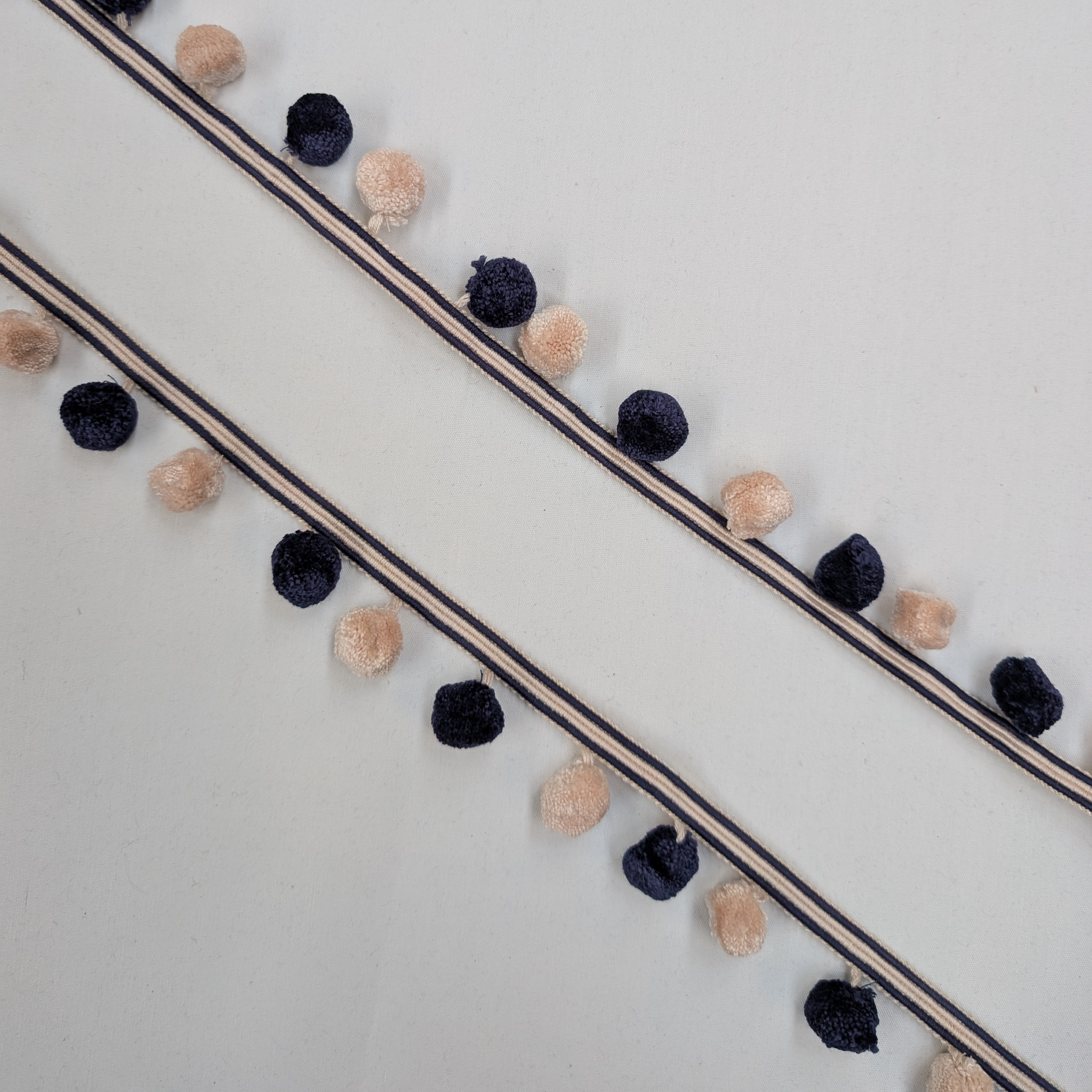 Decorative ribbon with navy and beige pom-poms on a white background