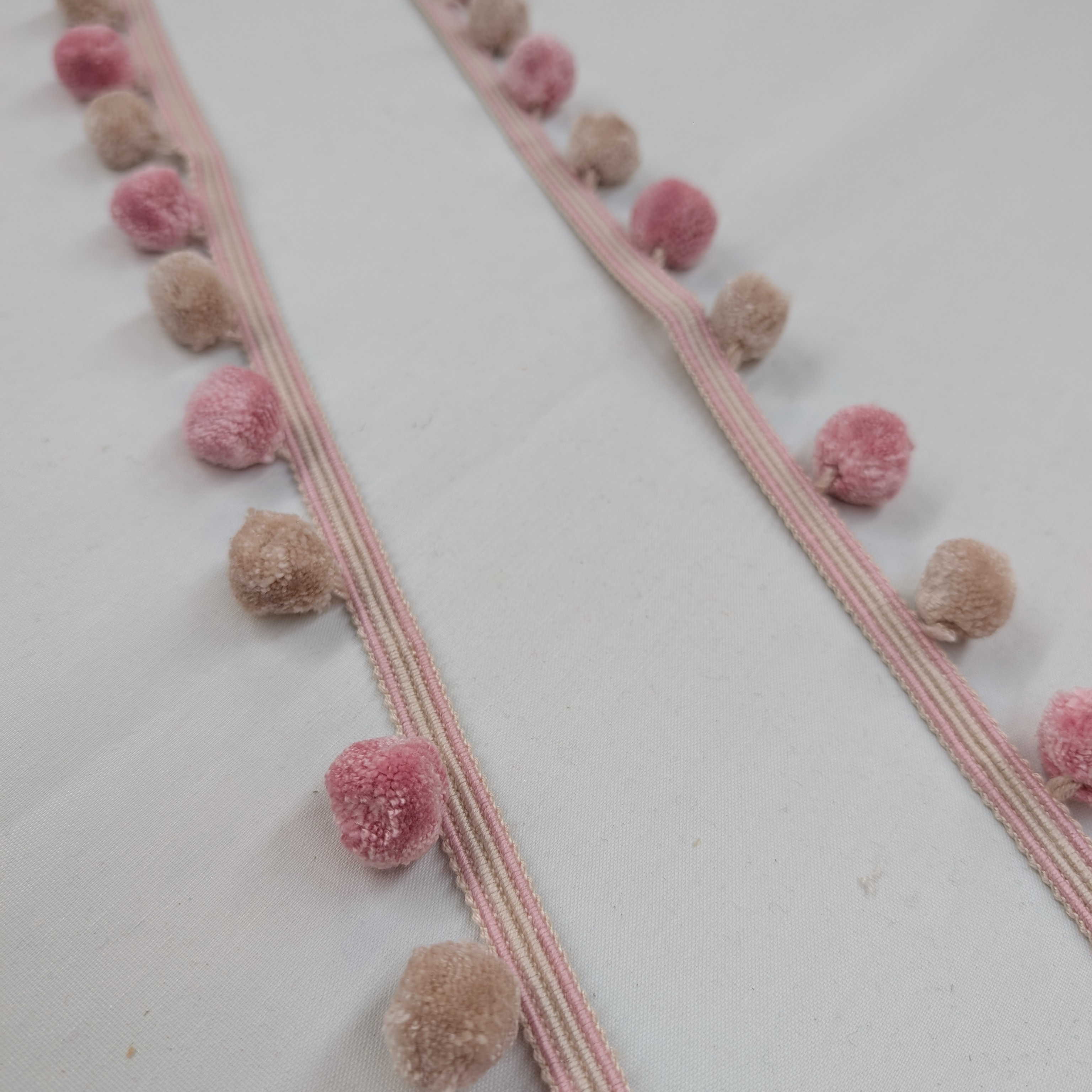 Stripes of pink and beige trim with pom-pom trim on a white background