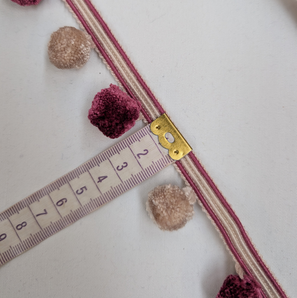 Decorative ribbon with pom-poms and a measuring tape on a white background