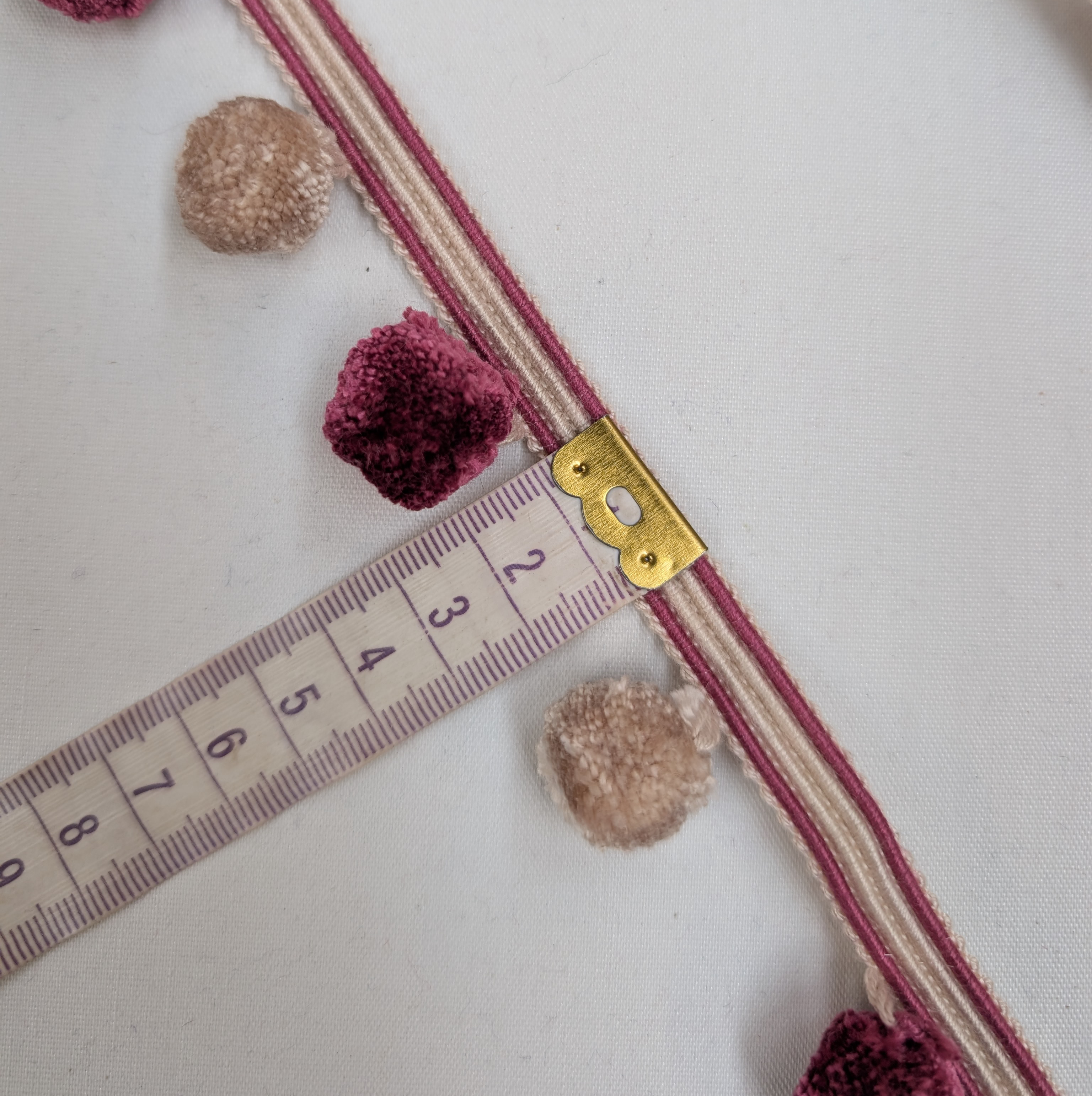 Decorative ribbon with pom-poms and a measuring tape on a white background