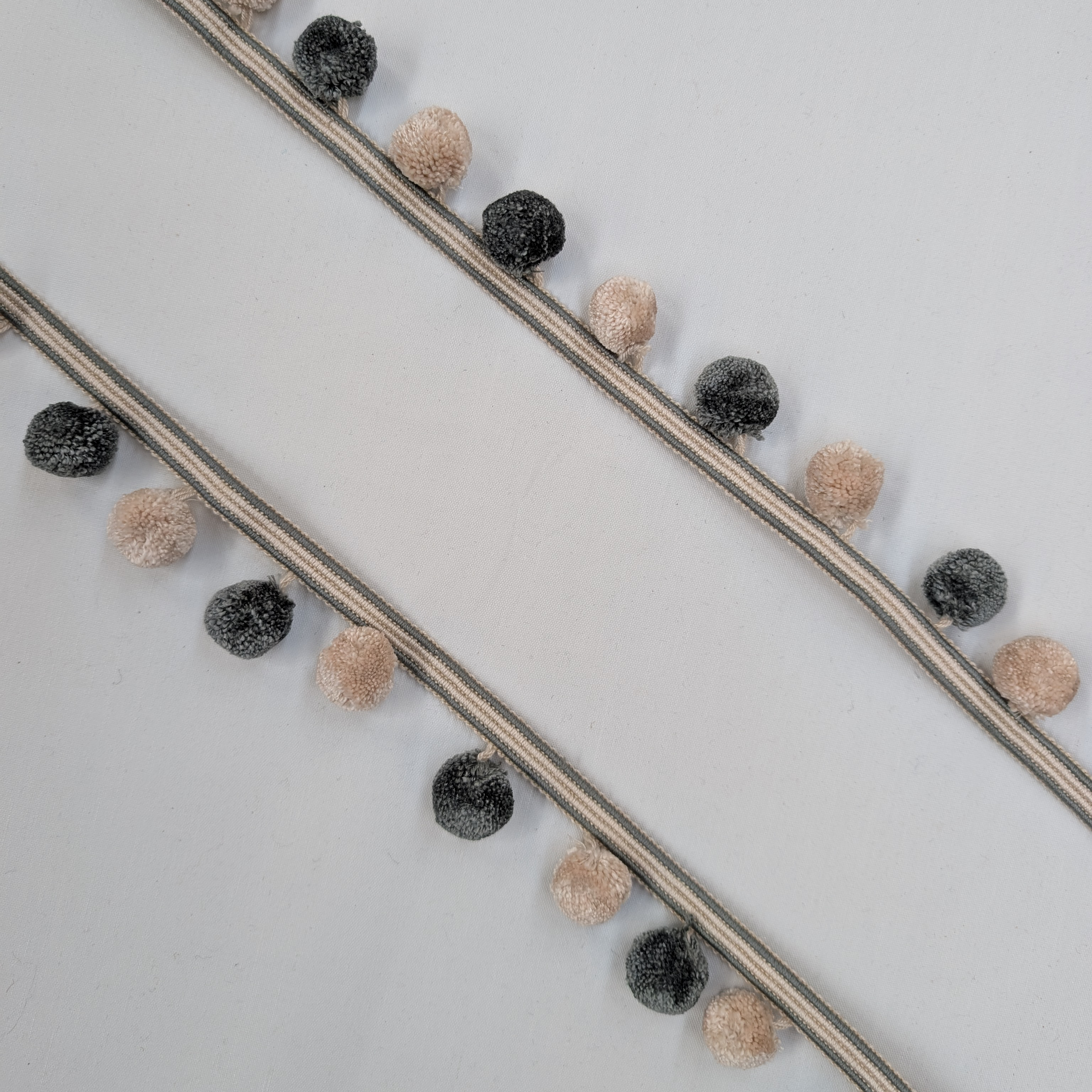 Decorative string with Green and beige pom-poms on a light gray background